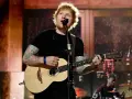 Ed Sheeran spielt Gitarre und singt auf einer Bühne.
