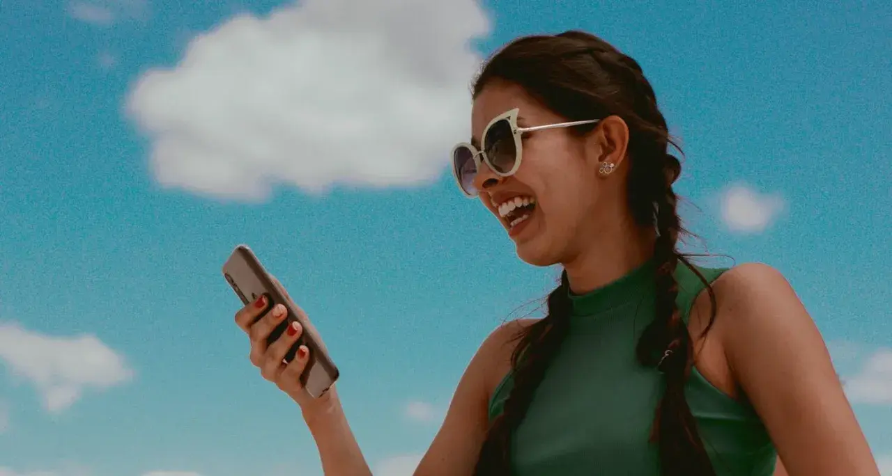Lachende Frau mit Sonnenbrille hält ein Smartphone. Sie hört Musik und fragt sich, wer singt das Lied.
