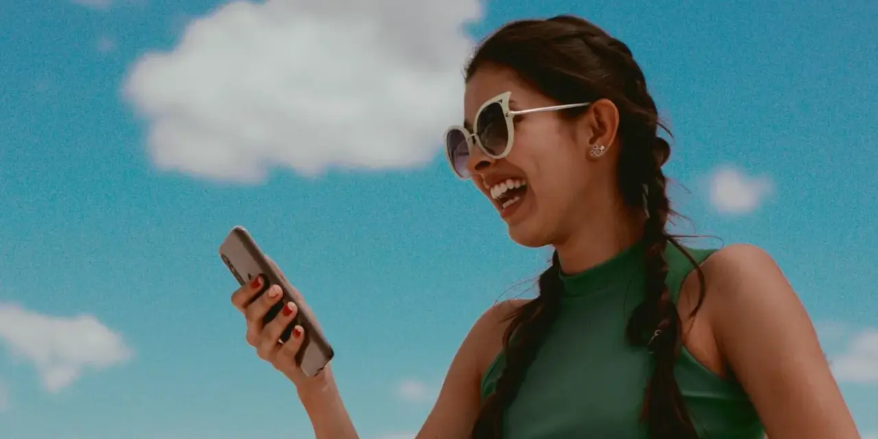 Lachende Frau mit Sonnenbrille hält ein Smartphone. Sie hört Musik und fragt sich, wer singt das Lied.