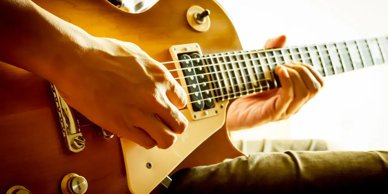 Hände spielen eine goldene E-Gitarre. Vielleicht ist das der Moment, in dem man sich entscheidet, eine E-Gitarre kaufen.