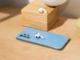 AirPods liegen auf einem blauen Samsung-Smartphone und einem Holzblock.