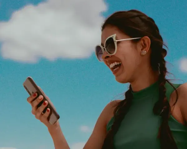 Lachende Frau mit Sonnenbrille hält ein Smartphone. Sie hört Musik und fragt sich, wer singt das Lied.