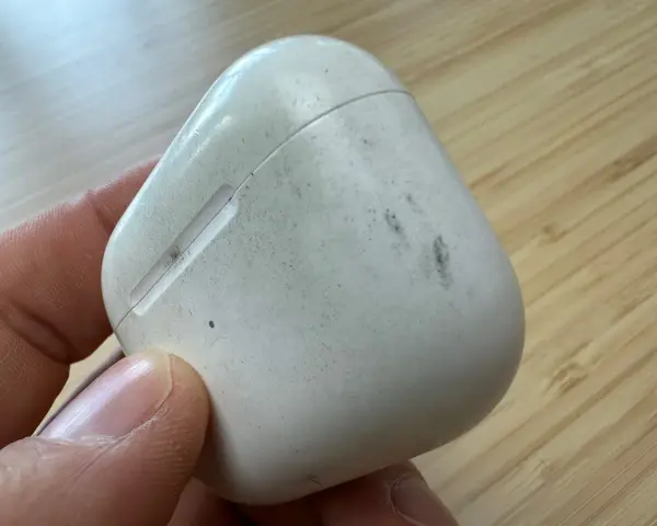 Eine schmutzige weiße Hülle für AirPods wird von einer Hand gehalten.