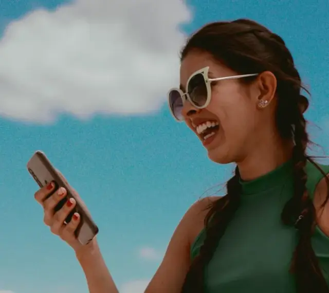 Lachende Frau mit Sonnenbrille hält ein Smartphone. Sie hört Musik und fragt sich, wer singt das Lied.