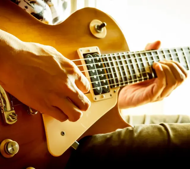 Hände spielen eine goldene E-Gitarre. Vielleicht ist das der Moment, in dem man sich entscheidet, eine E-Gitarre kaufen.
