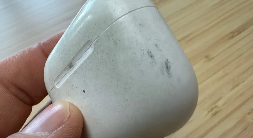Eine schmutzige weiße Hülle für AirPods wird von einer Hand gehalten.