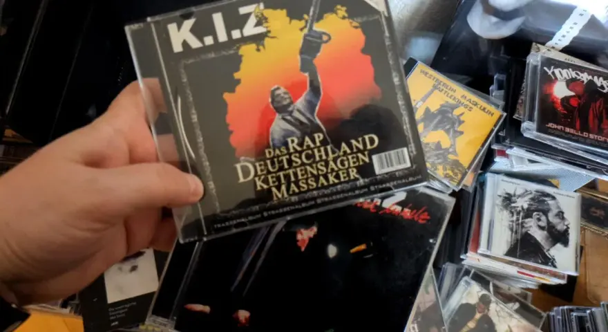Hand hält CD-Cover von K.I.Z. "Das Rap Deutschland Kettensägen Massaker" mit Kettensäge.