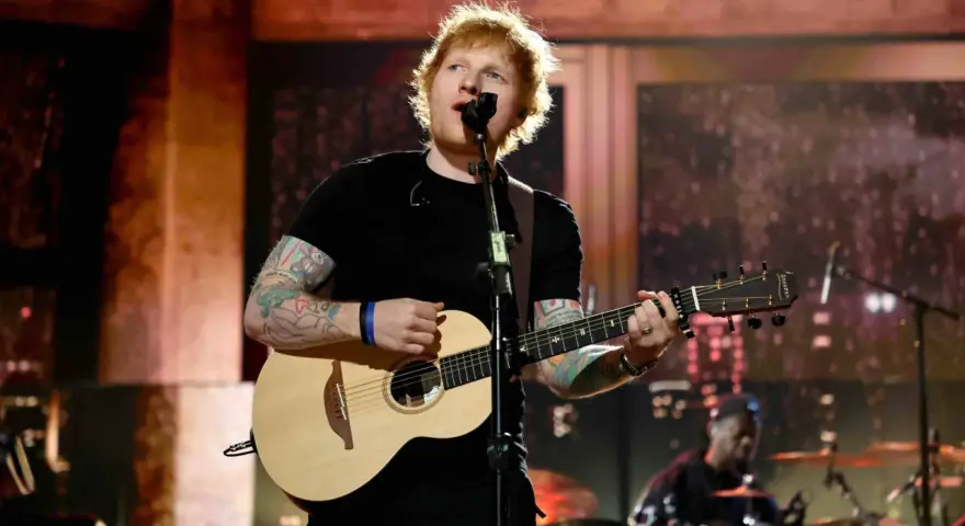 Ed Sheeran spielt Gitarre und singt auf einer Bühne.