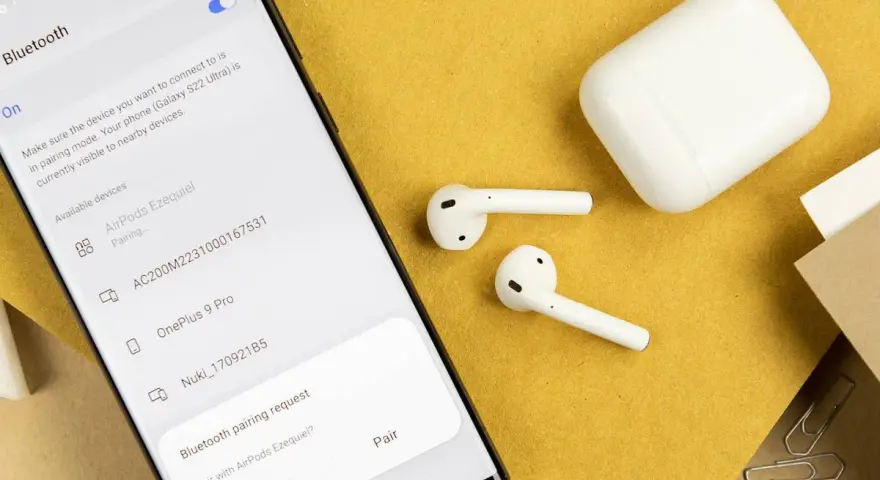 Samsung-Smartphone zeigt Bluetooth-Kopplungsanfrage für AirPods an, daneben liegen AirPods und Ladecase.