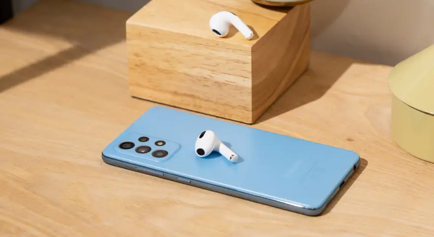 AirPods liegen auf einem blauen Samsung-Smartphone und einem Holzblock.