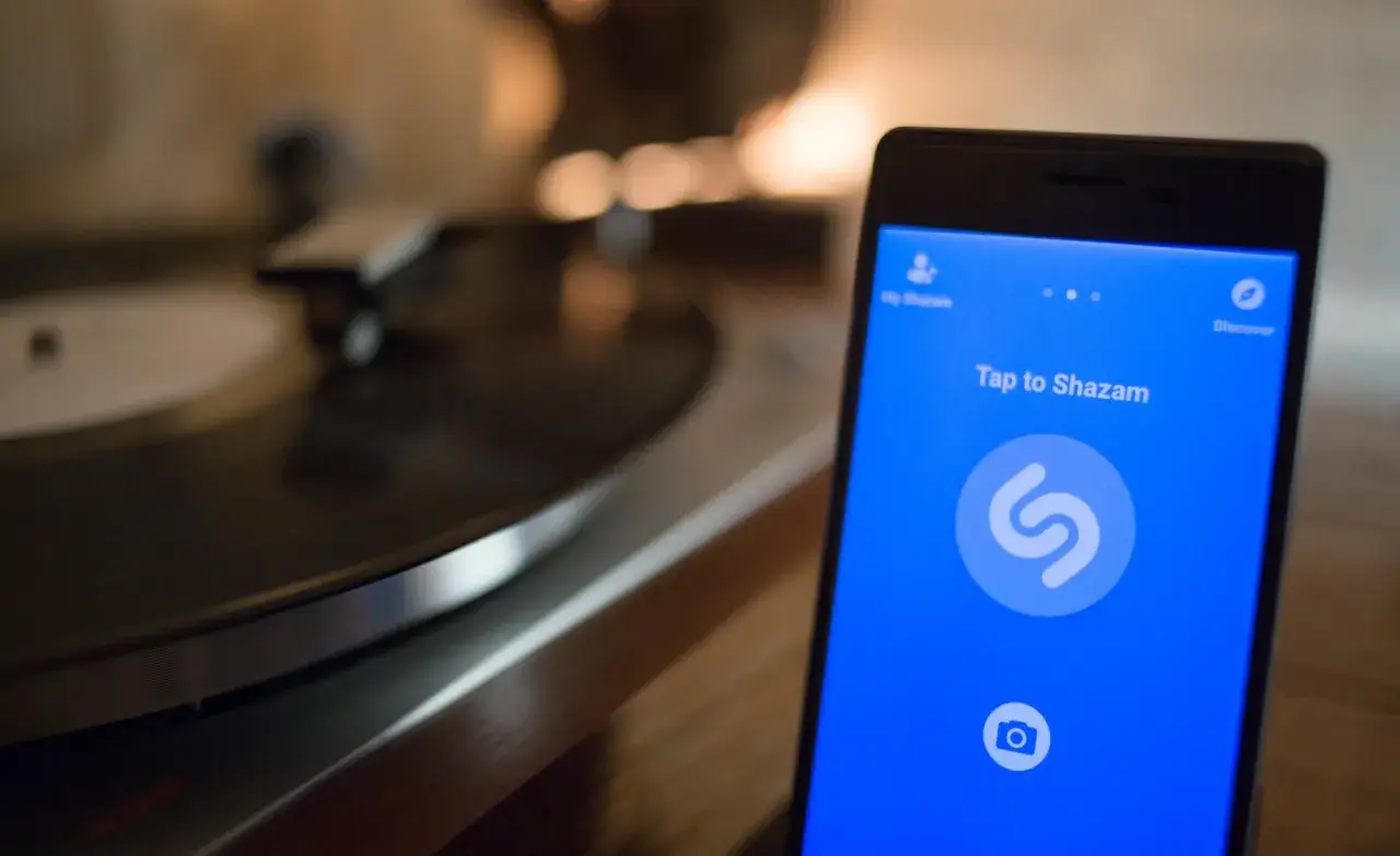 Ein Smartphone mit der Shazam-App, bereit, zu erkennen, wer singt dieses Lied. Im Hintergrund dreht sich eine Schallplatte.