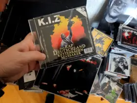 Hand hält CD-Cover von K.I.Z. "Das Rap Deutschland Kettensägen Massaker" mit Kettensäge.