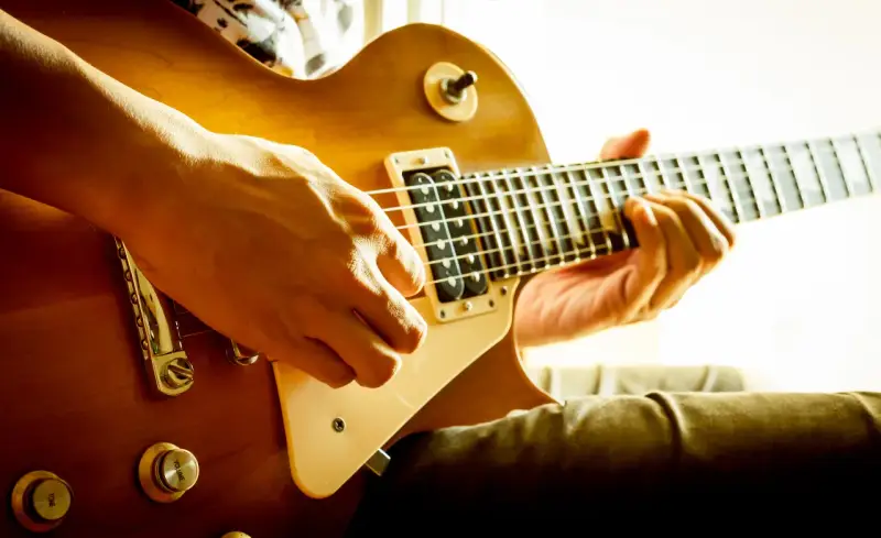 Hände spielen eine goldene E-Gitarre. Vielleicht ist das der Moment, in dem man sich entscheidet, eine E-Gitarre kaufen.